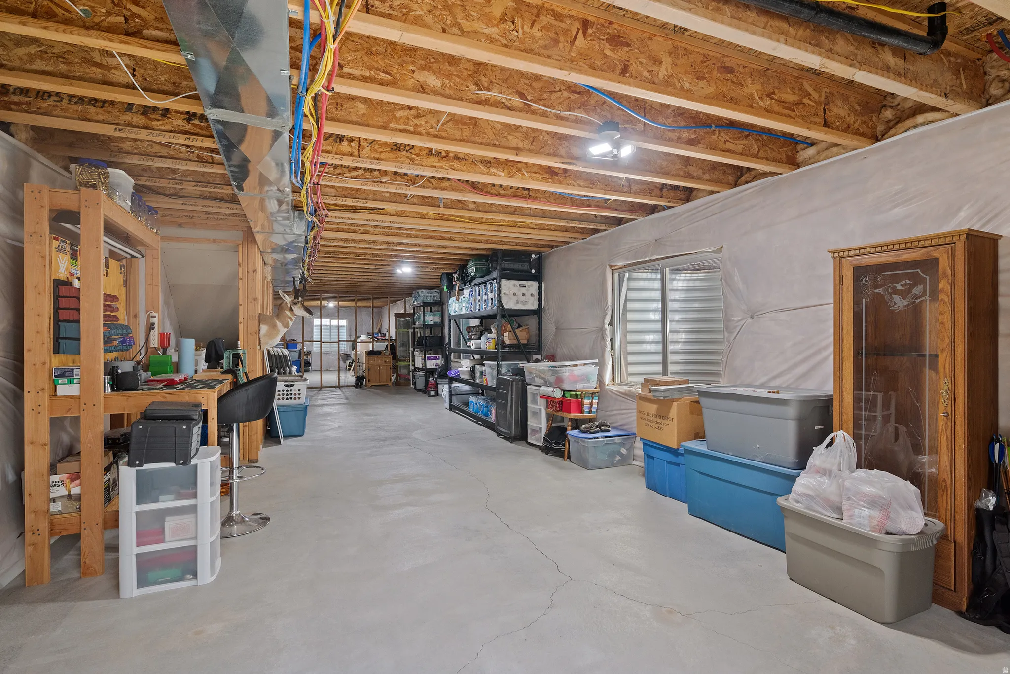 Unfinished basement featuring exposed wood joists, concrete flooring, and an egress window