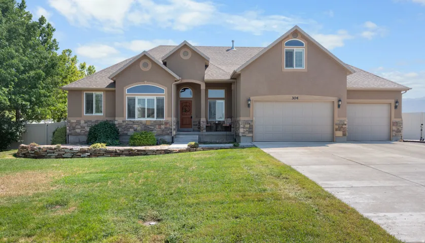Stucco exterior with stone accents, a multi-car garage, arched window features, and a stone retaining wall