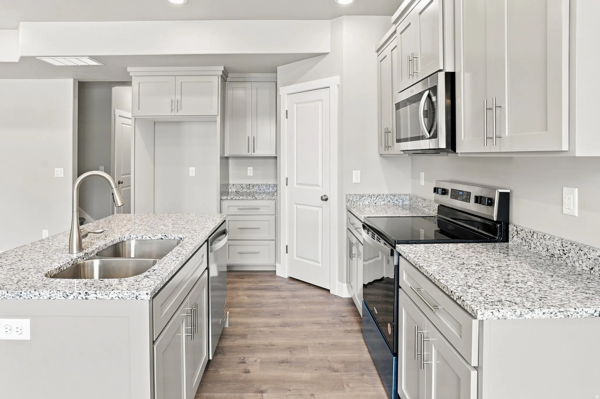 Kitchen featuring light grey cabinetry, stone-finish countertops, stainless steel appliances, and wood-finish flooring