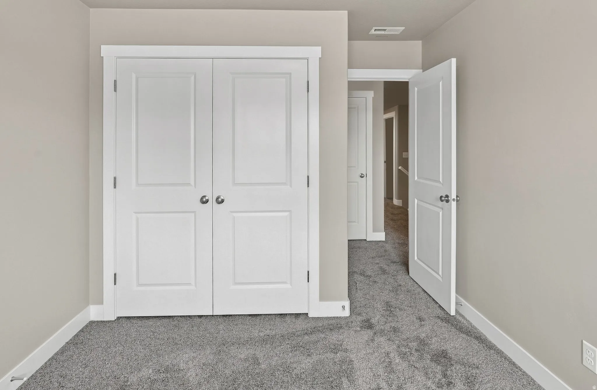Neutral-toned wall finish, white trim, grey carpeting, and white panel doors