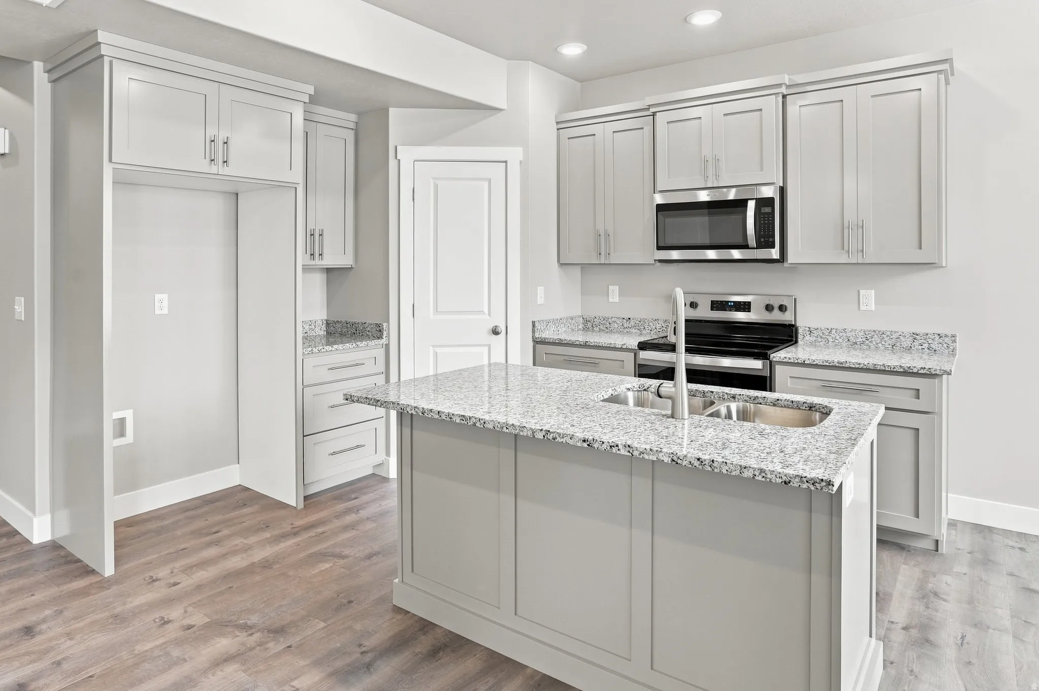 Kitchen featuring wood-finish flooring, light-toned cabinetry, a central island with an undermount sink, stainless steel appliances, and stone countertops