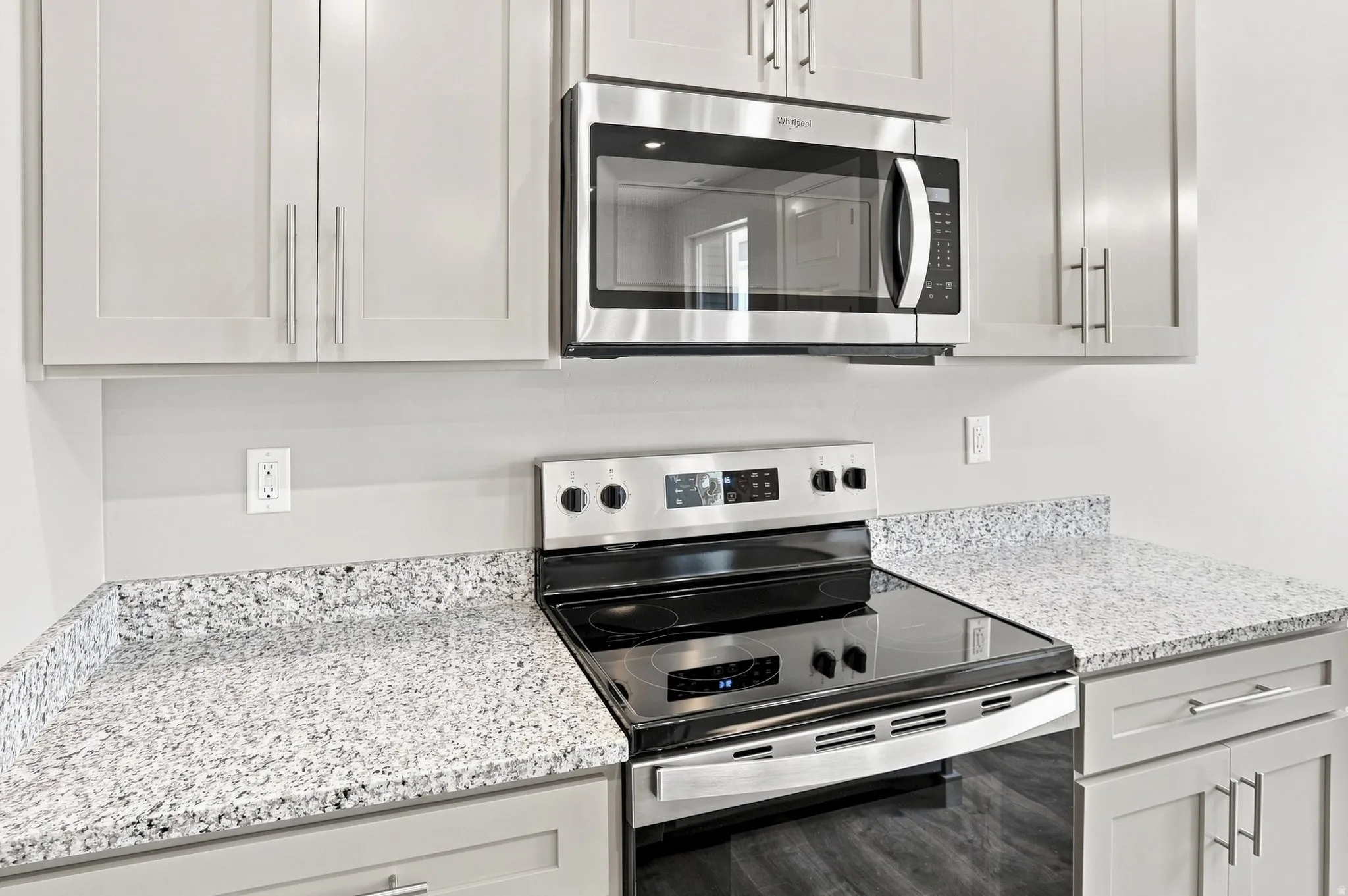 Light-toned cabinetry with stainless hardware, stone-finish countertops, stainless steel electric range, and an over-the-range microwave