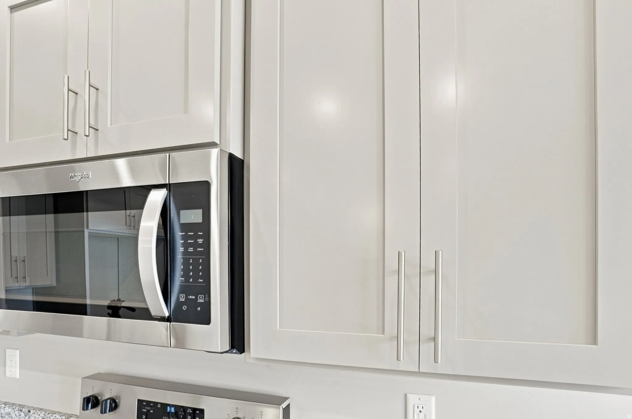 White shaker-style cabinetry with brushed nickel hardware, stainless steel over-the-range microwave, and light-colored countertops
