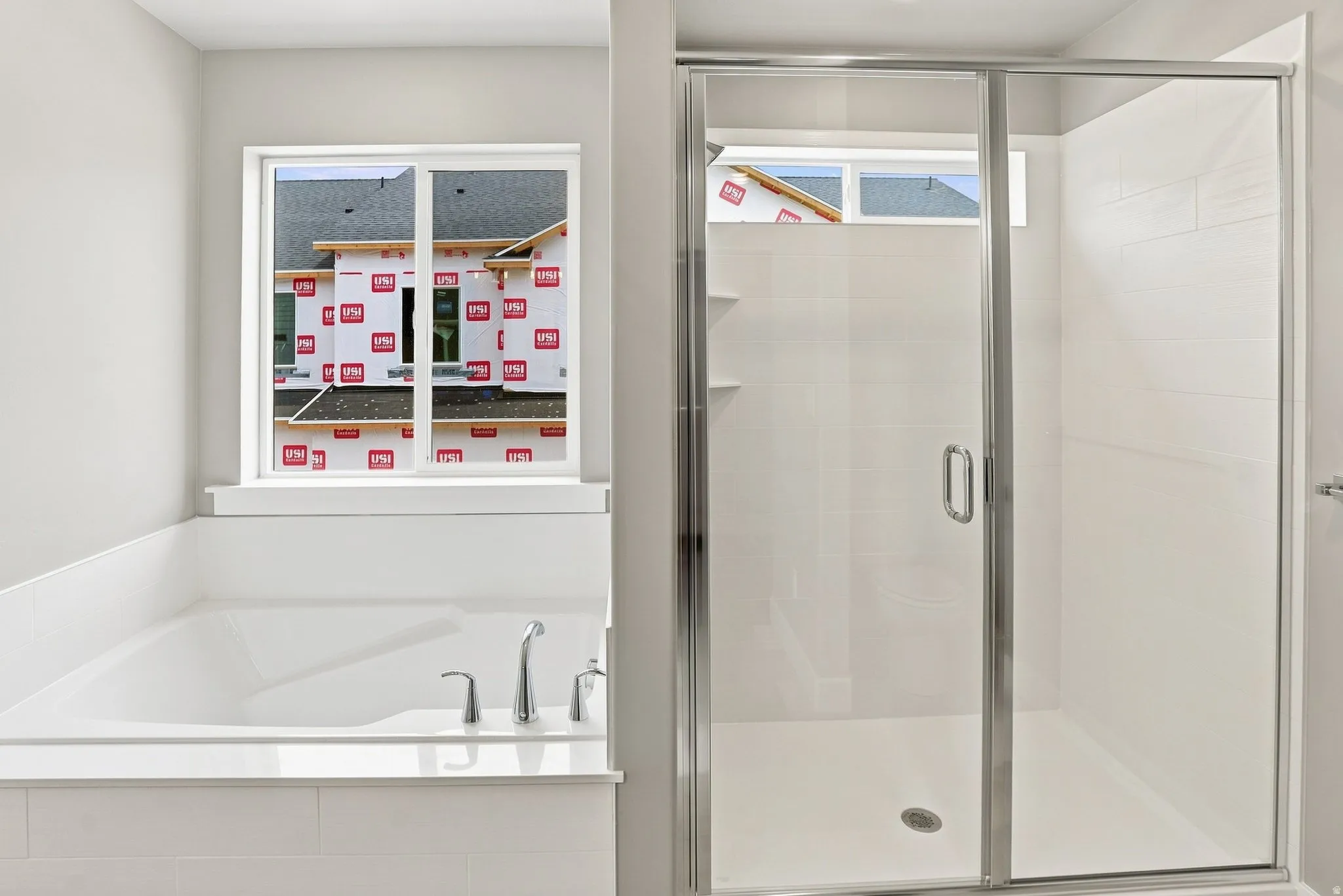 Soaking tub with deck-mounted chrome fixtures, adjacent to a glass-enclosed shower with white tiled walls and built-in shelving