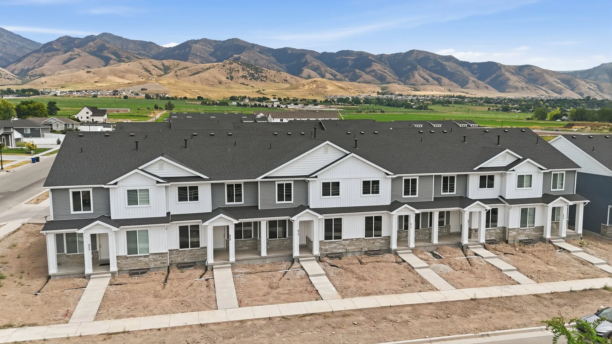 Townhome community featuring white and gray siding with stone accents, covered front entryways, dark shingle roofs, and concrete walkways