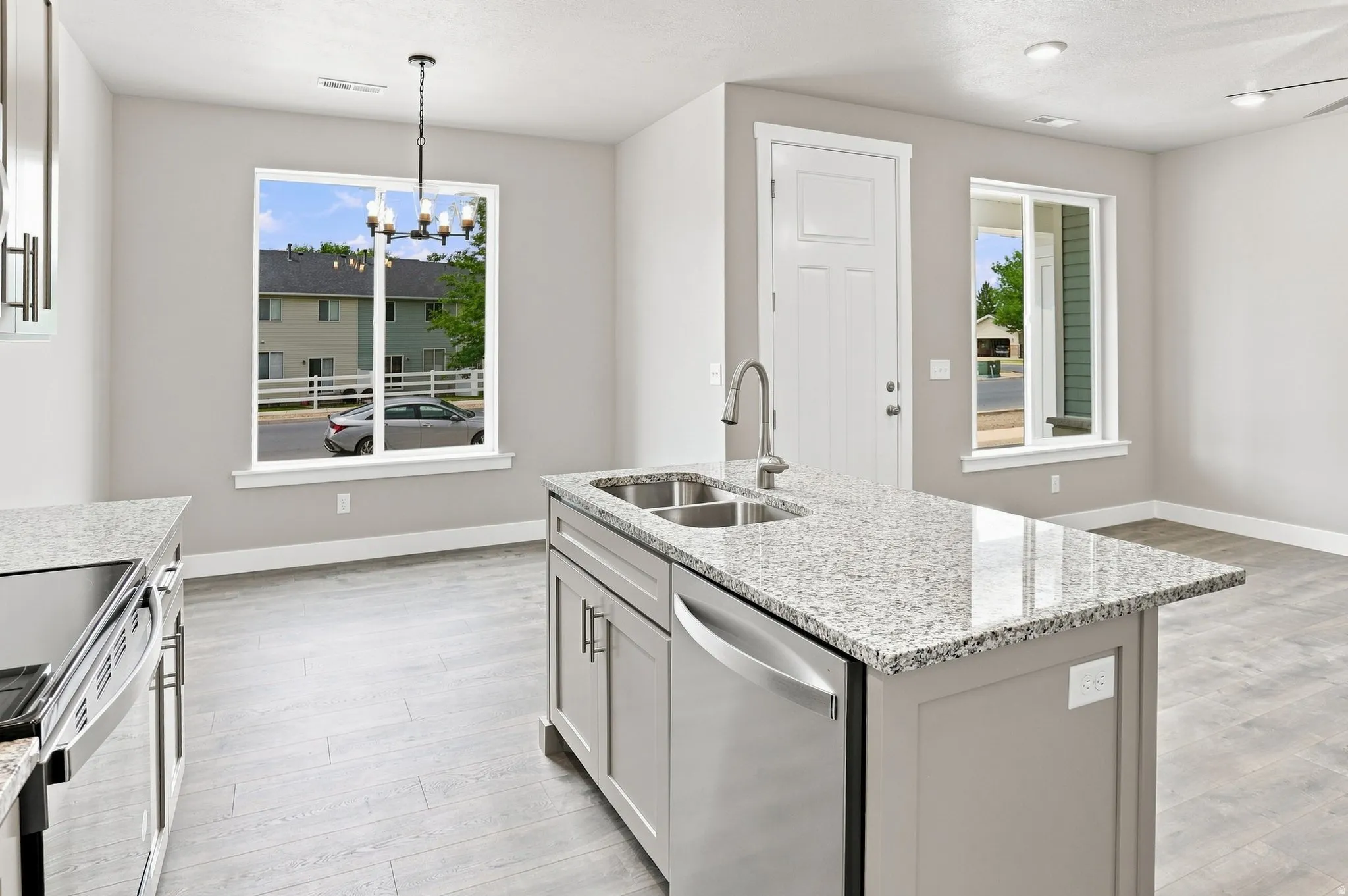 Kitchen featuring an island with double stainless steel sink, granite countertops, and wood-finish flooring