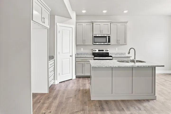 Kitchen featuring wood-finish flooring, recessed lighting, a kitchen island with sink, gray cabinetry, and light-colored countertops
