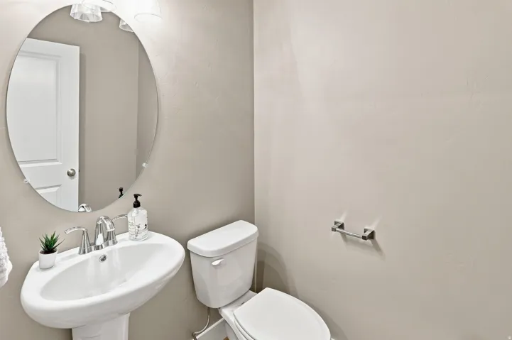 Pedestal sink with chrome faucet, oval mirror, and overhead vanity lighting