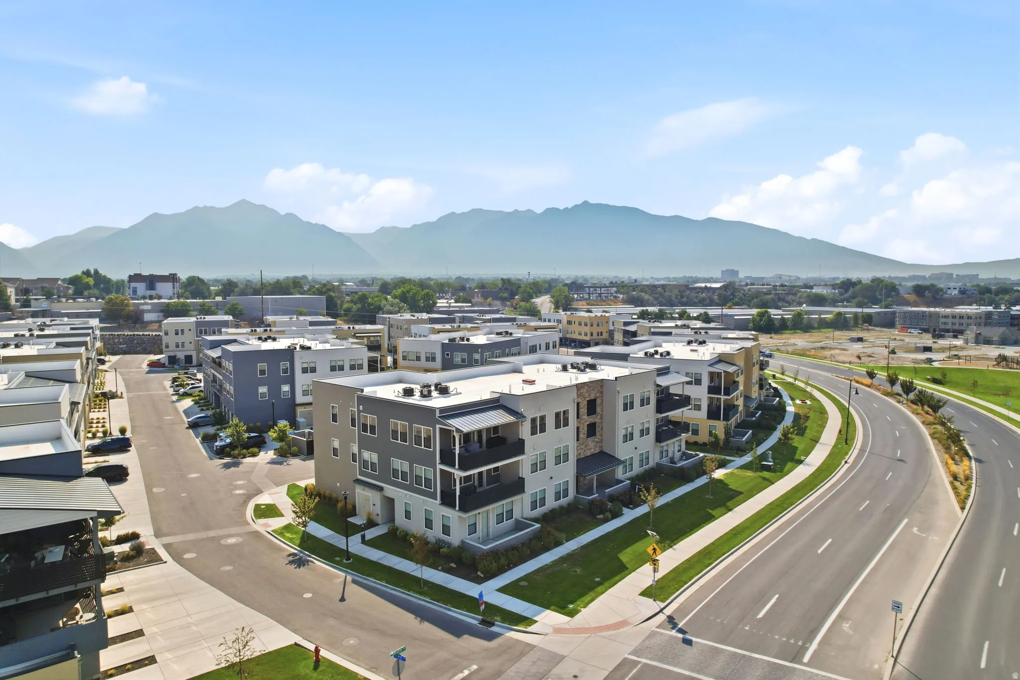 Modern multi-story buildings with balconies, paved roadways, and landscaped green spaces, all set against a mountain backdrop