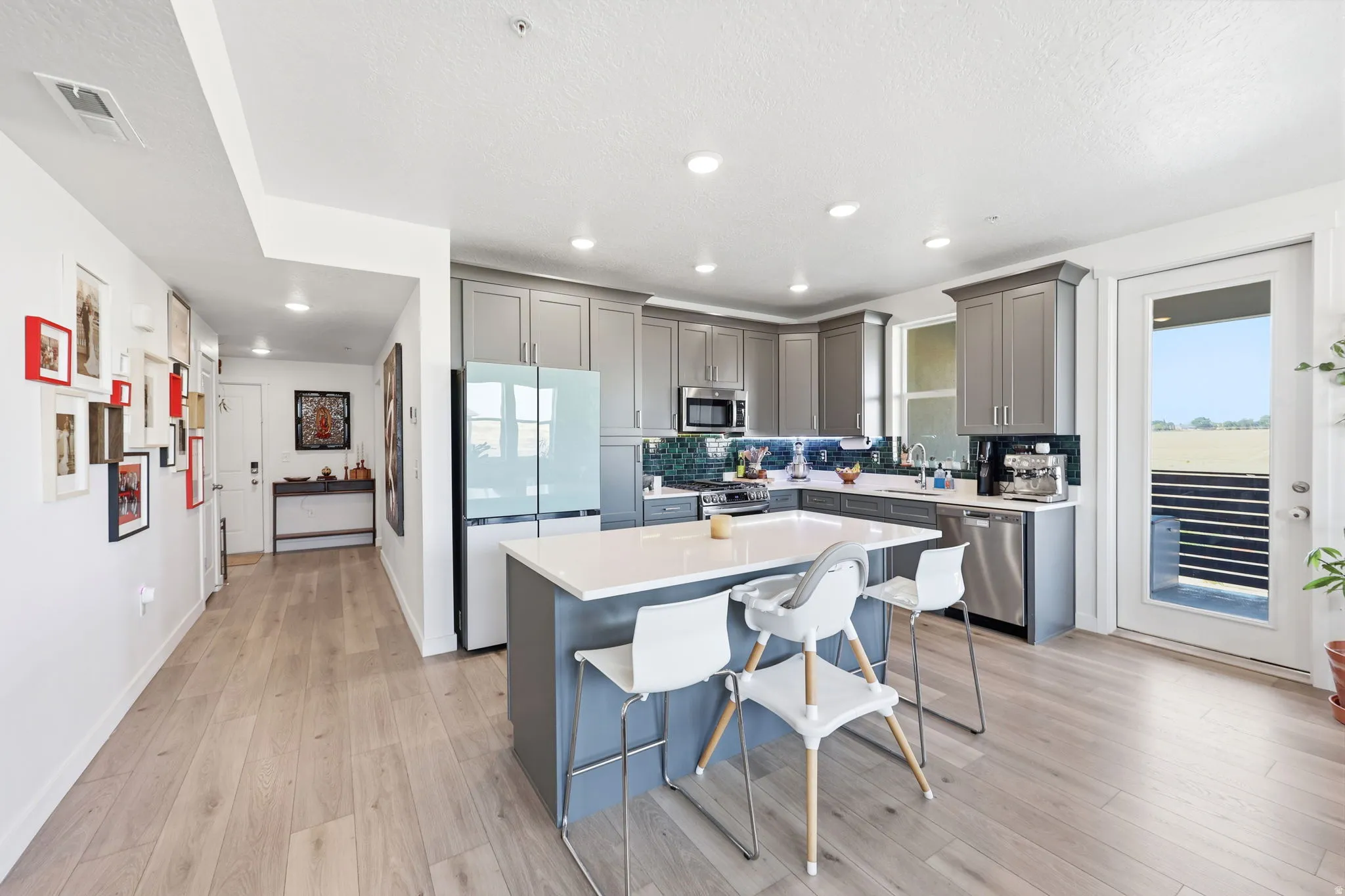 Kitchen featuring grey cabinetry, stainless steel appliances, a center island with countertop seating, wood-finish flooring, and a glass-paneled exterior door