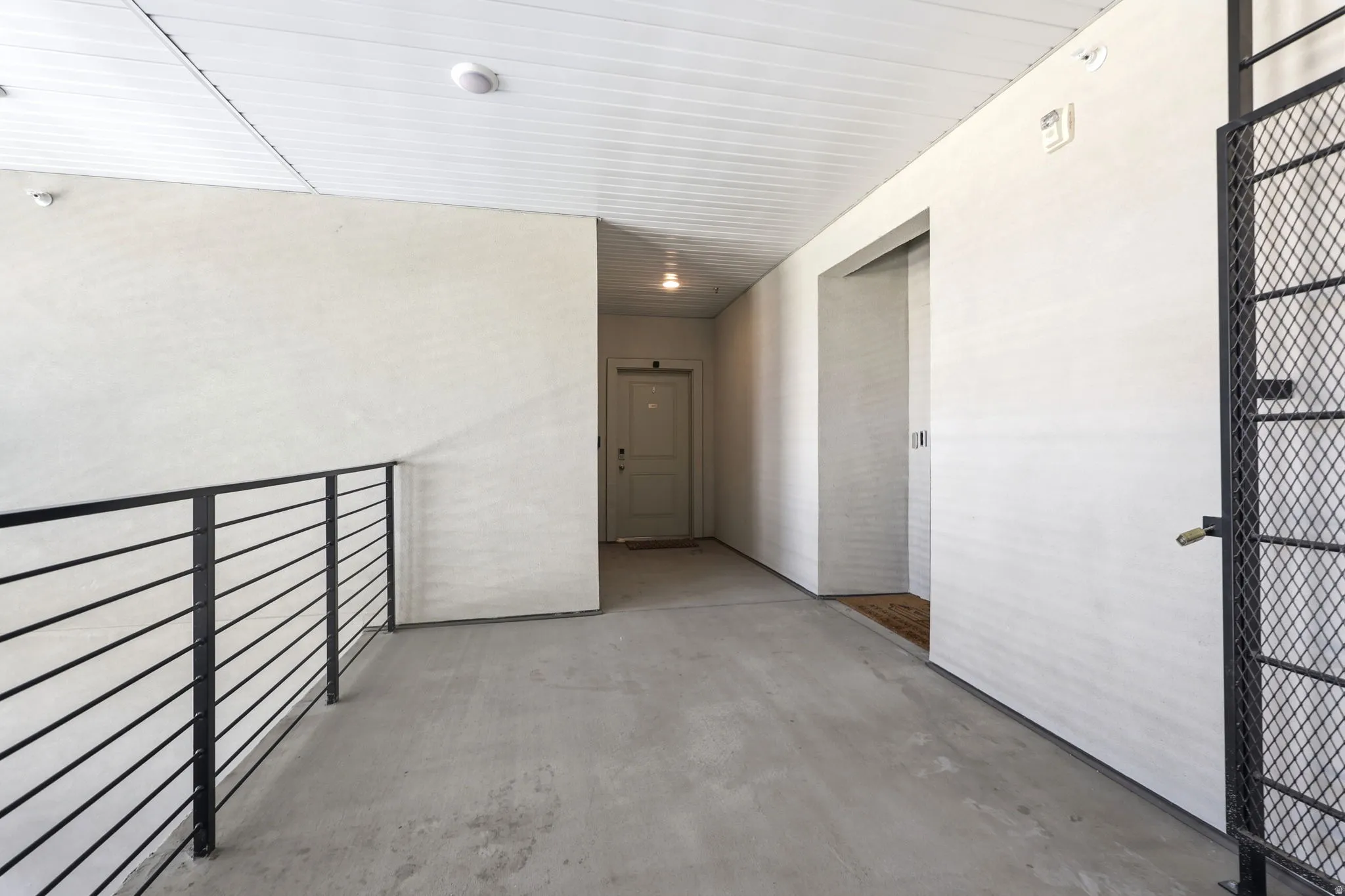 Concrete flooring, white walls, black metal horizontal bar railing, black metal mesh gate, white panel ceiling