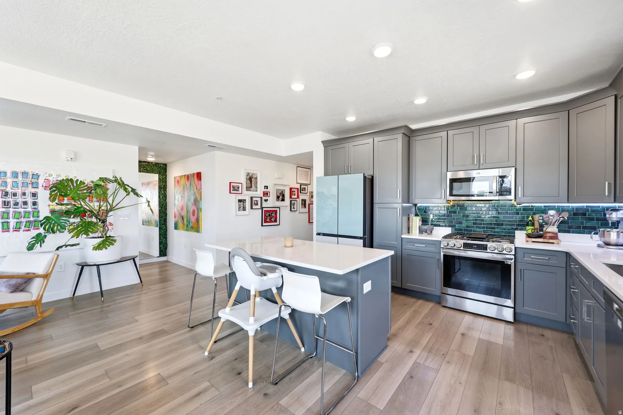 Kitchen featuring gray cabinetry, stainless steel appliances, a teal tile backsplash, and a central island with countertop seating