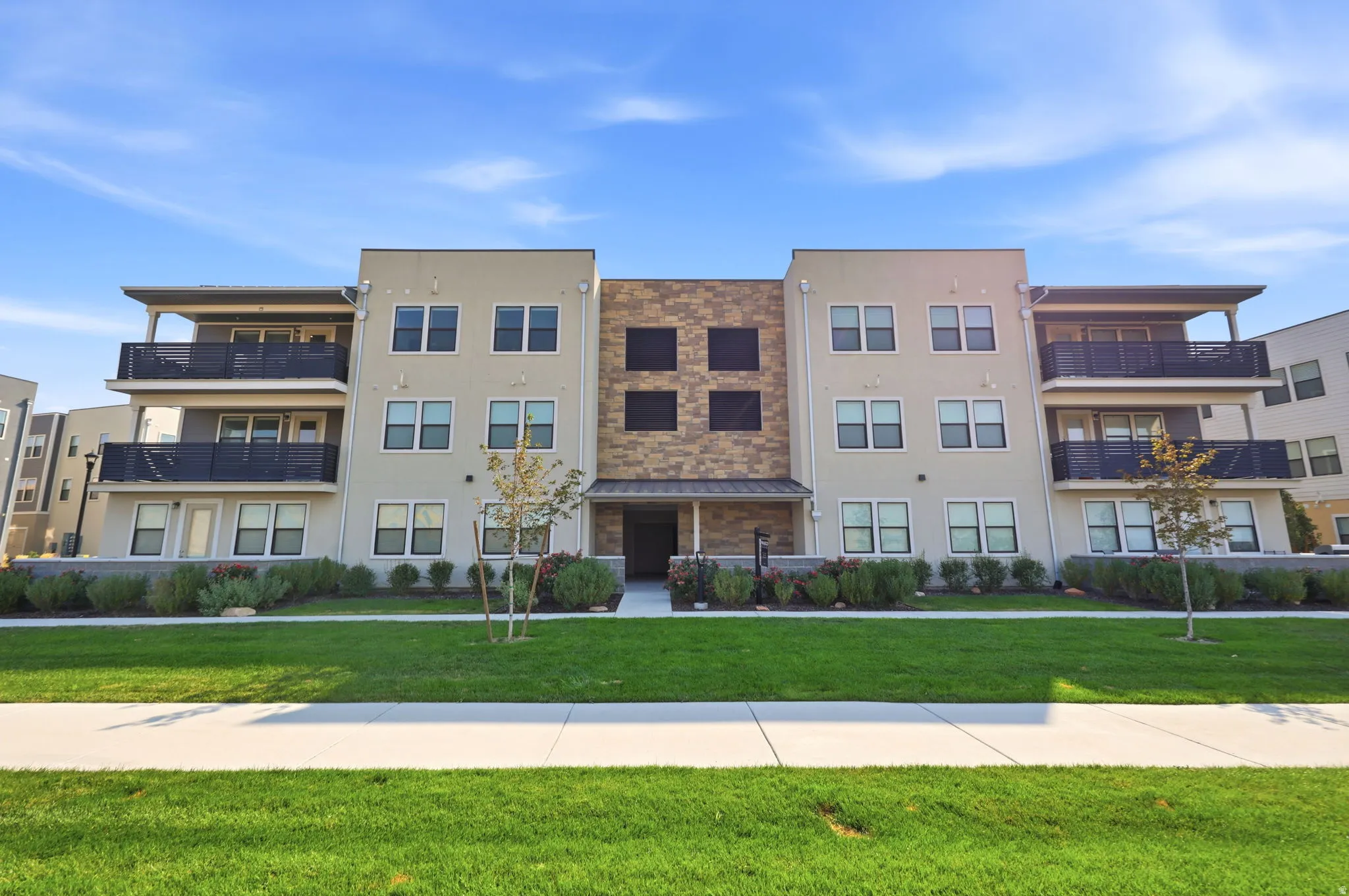 Modern multi-story building featuring a stucco exterior, stone facade accents, private balconies, and an entry portico