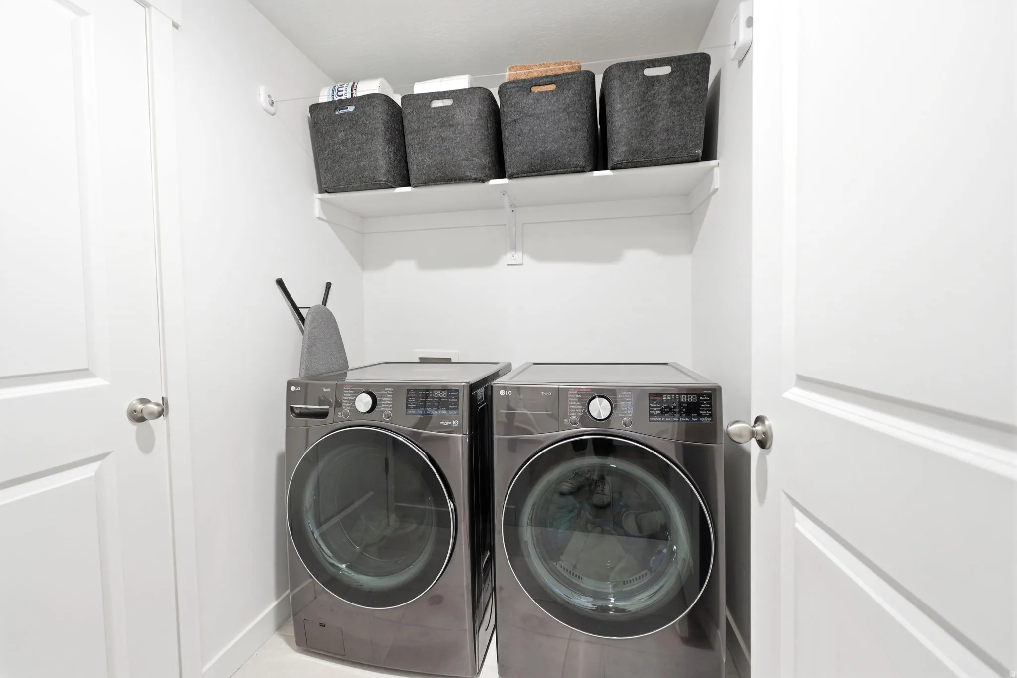 Integrated laundry closet with white shelving and a modern washer and dryer