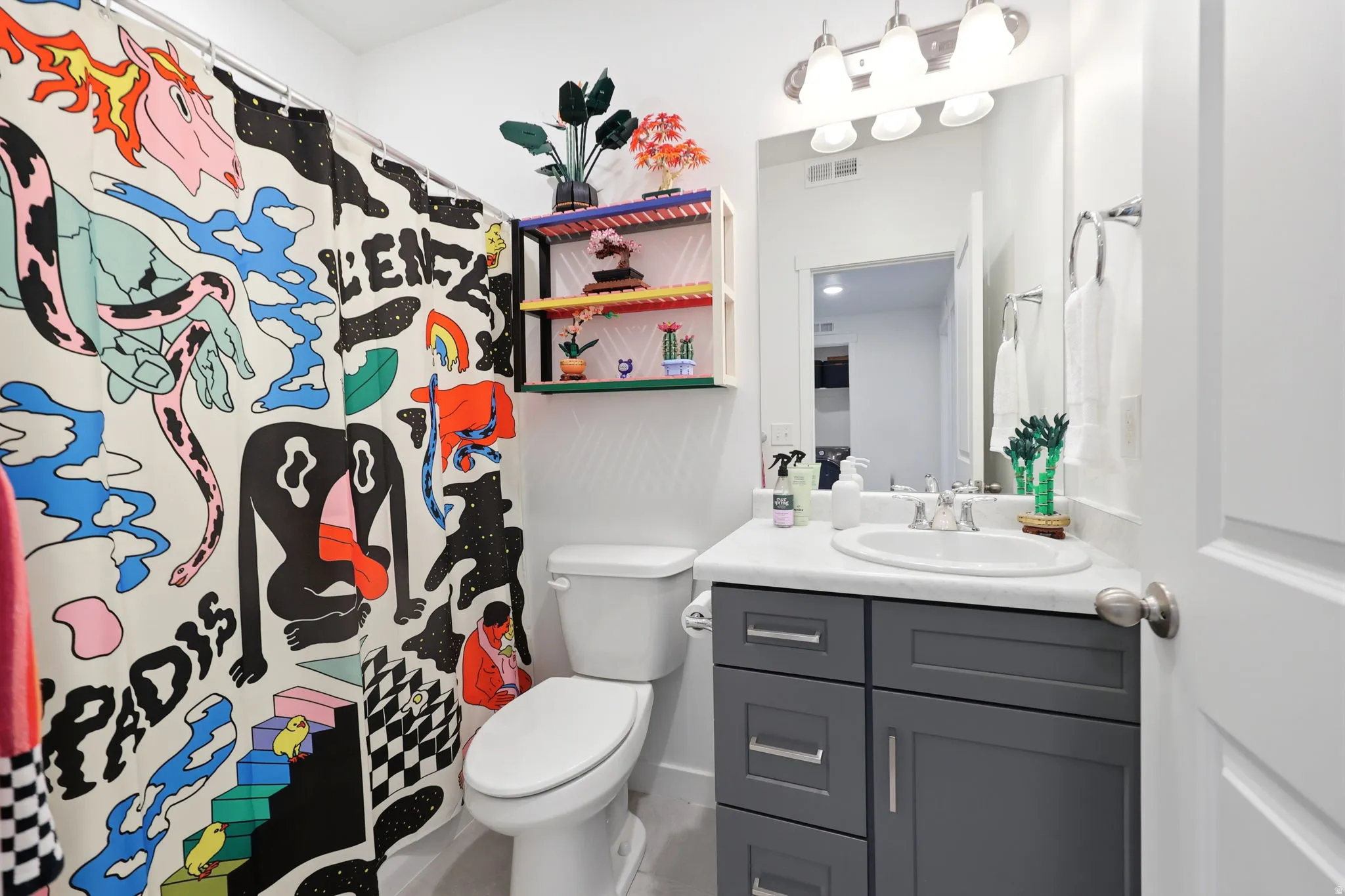 Bathroom featuring a white toilet, gray vanity with silver hardware, recessed sink, and a wall-mounted light fixture