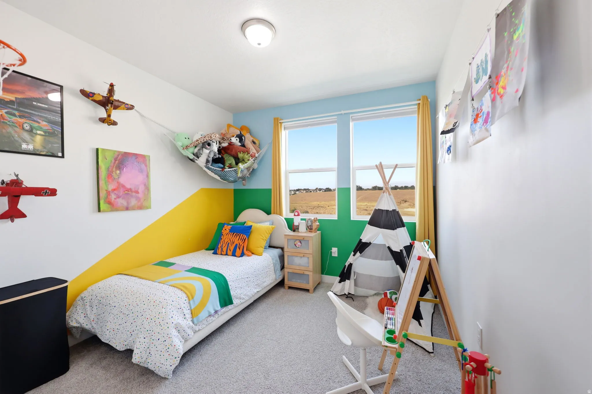 Dual windows with yellow drapes, light-colored carpeting, white walls with color block accents, and a flush mount ceiling light