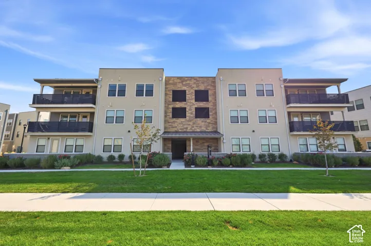 Modern multi-story building featuring a stucco exterior, stone facade accents, private balconies, and an entry portico