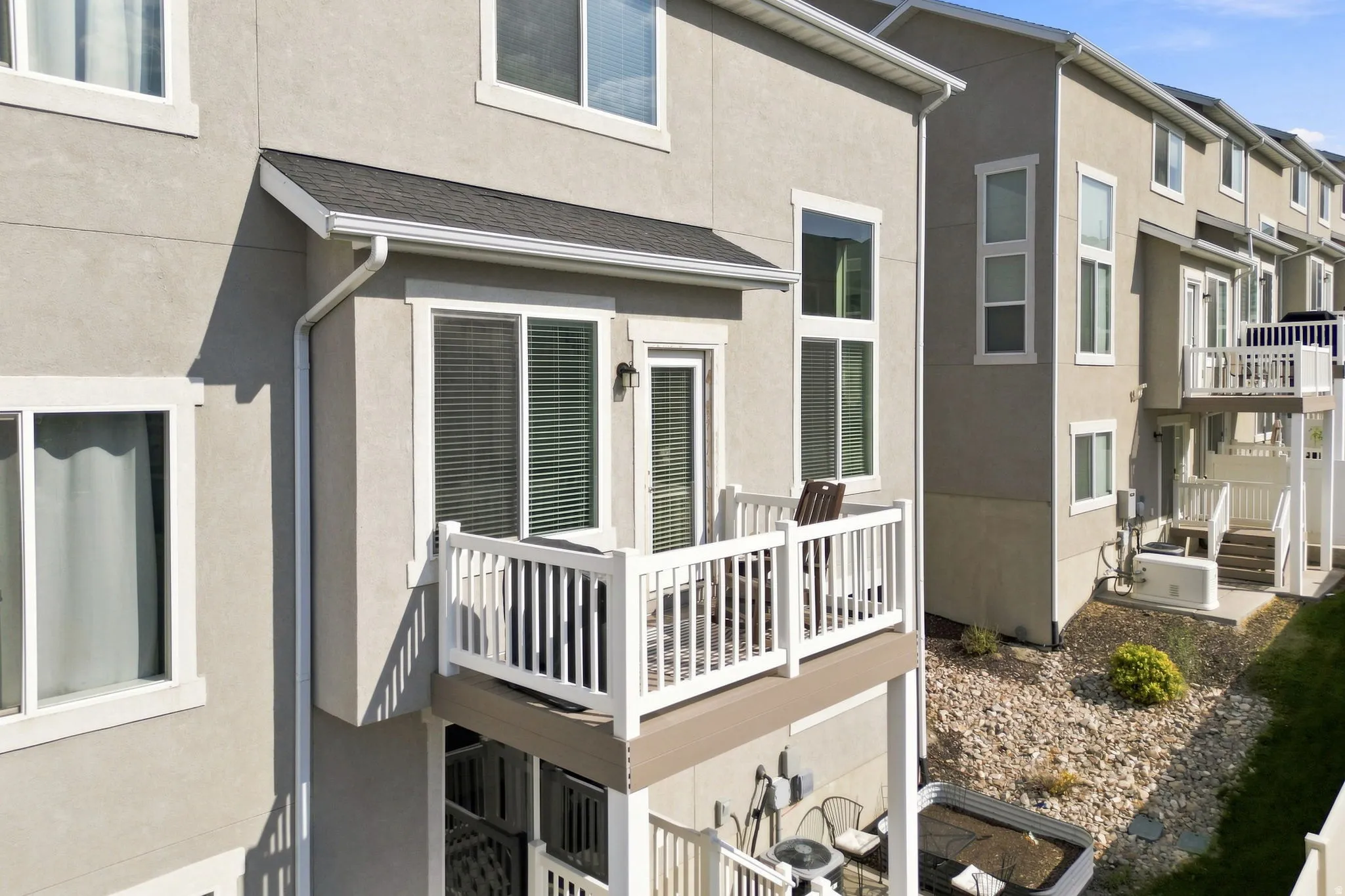 Stucco exterior featuring multiple windows, white balcony railings, and a lower-level patio