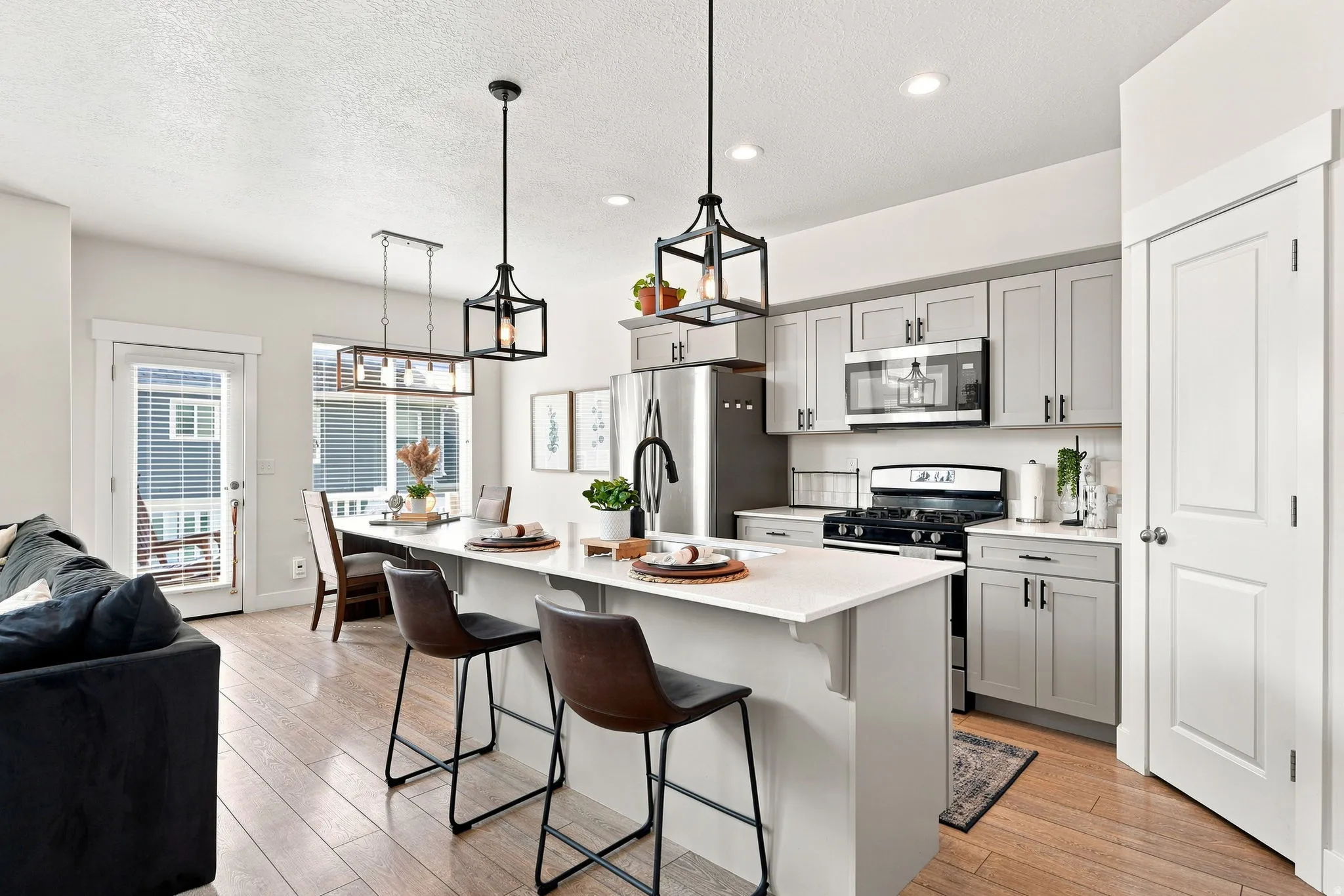 Open-concept kitchen featuring an island with counter seating, stainless steel appliances, light gray cabinetry, and wood-finish flooring