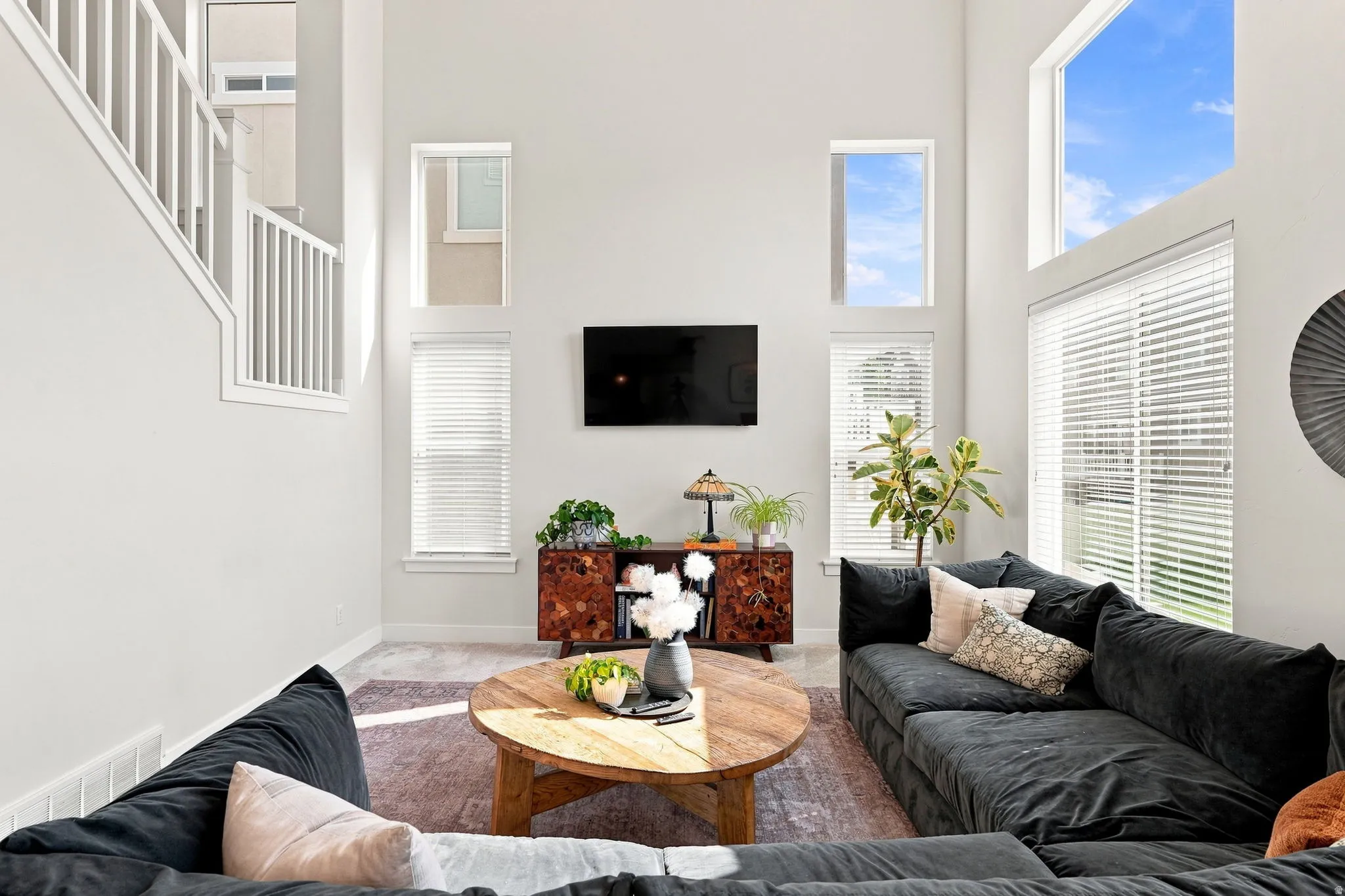 Vaulted ceiling with high windows, wood-finish console cabinet, and stairwell with white railings