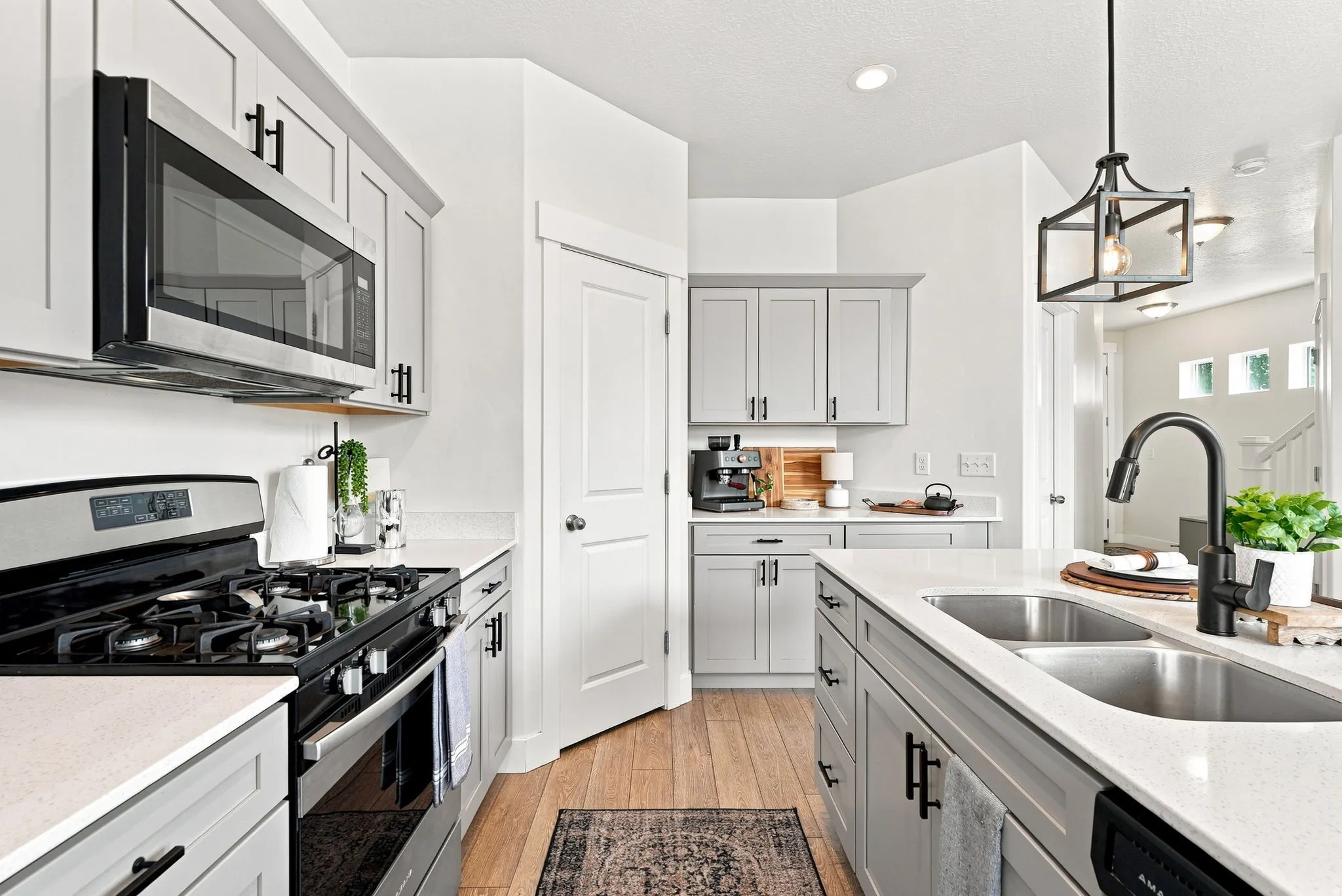 Kitchen featuring light gray shaker cabinets, stainless steel appliances, white countertops, wood-finish flooring, and a double basin sink with a matte black faucet