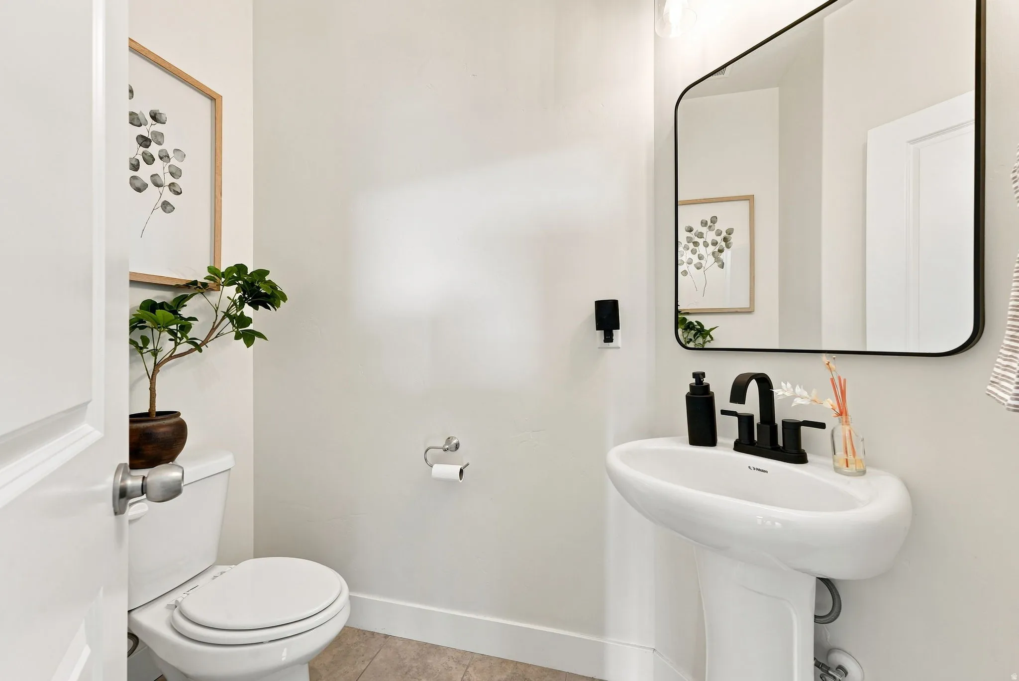 Pedestal sink with matte black faucet, wall-mounted mirror with rounded corners, and tile flooring