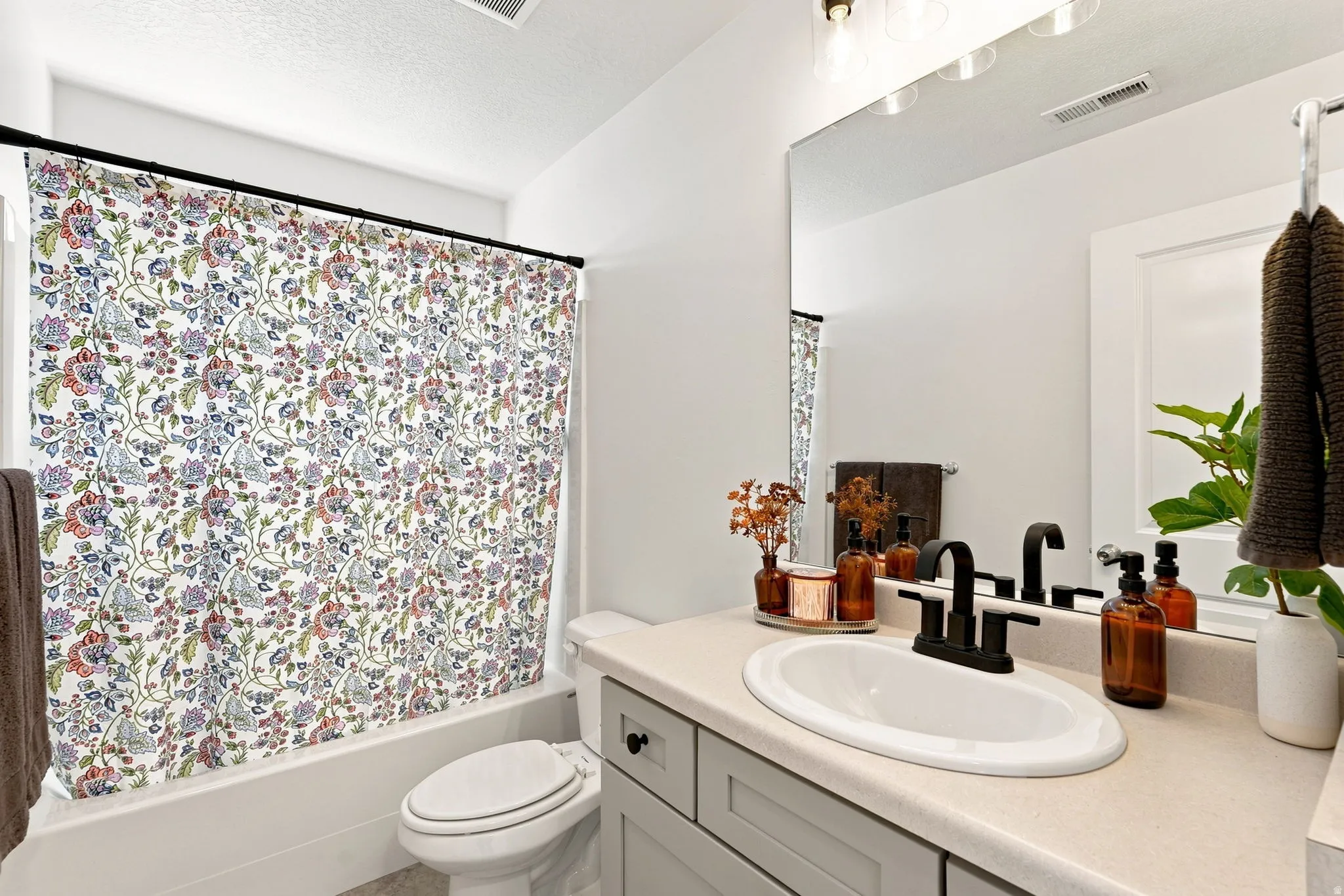 Bathroom featuring a light-toned vanity with dark hardware, an integrated sink, a large wall-mounted mirror, and a bathtub with a shower