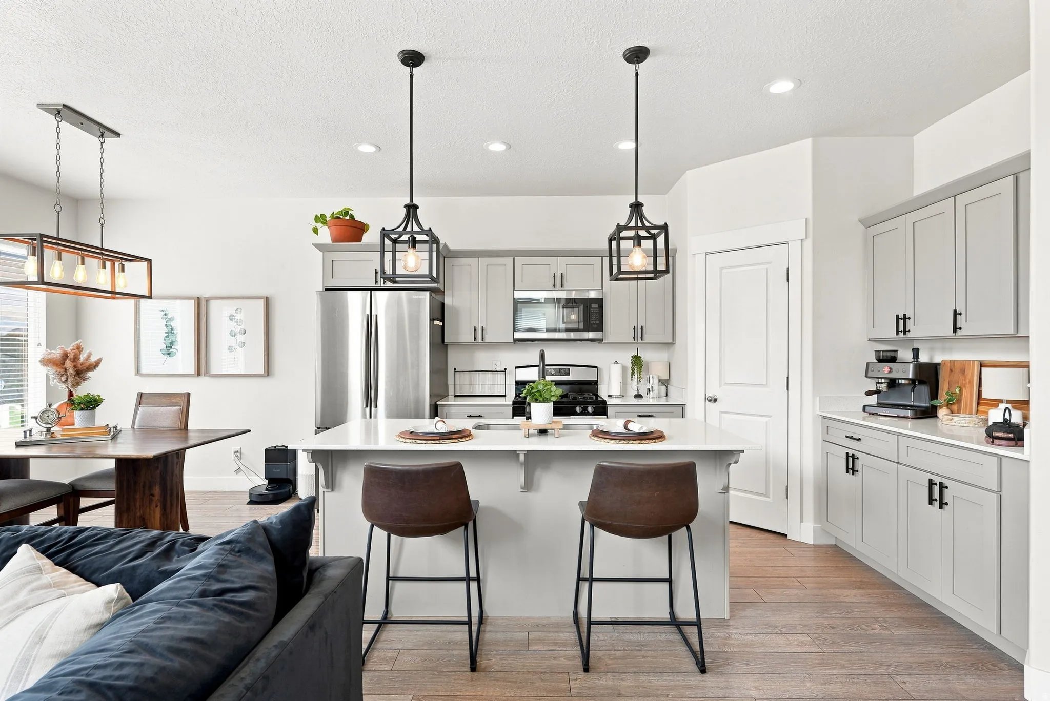 Modern kitchen featuring light gray cabinetry, stainless steel appliances, a center island with pendant lighting, and wood-finish flooring