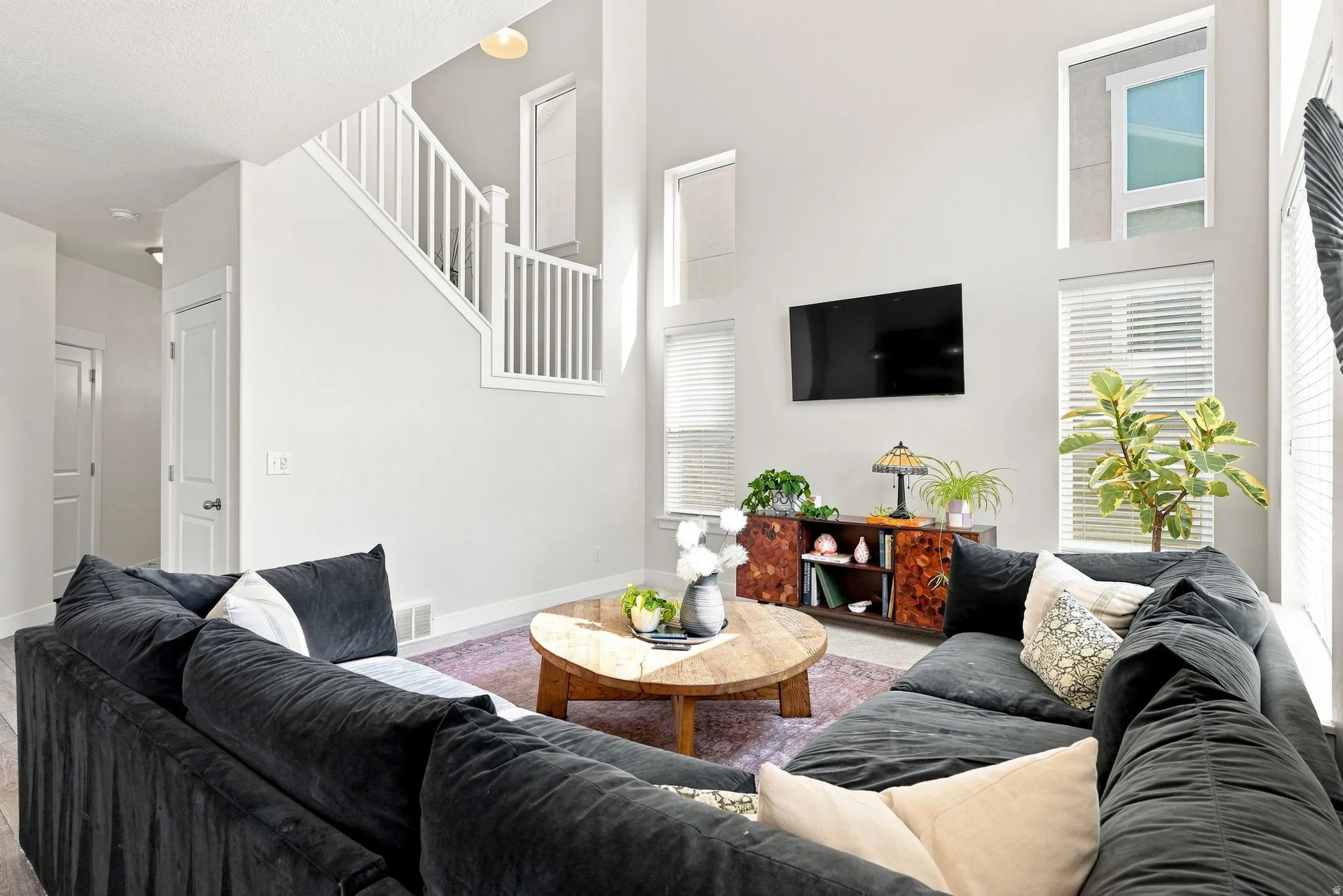 Two-story living area with high ceilings, multiple windows, and a built-in staircase with white balusters