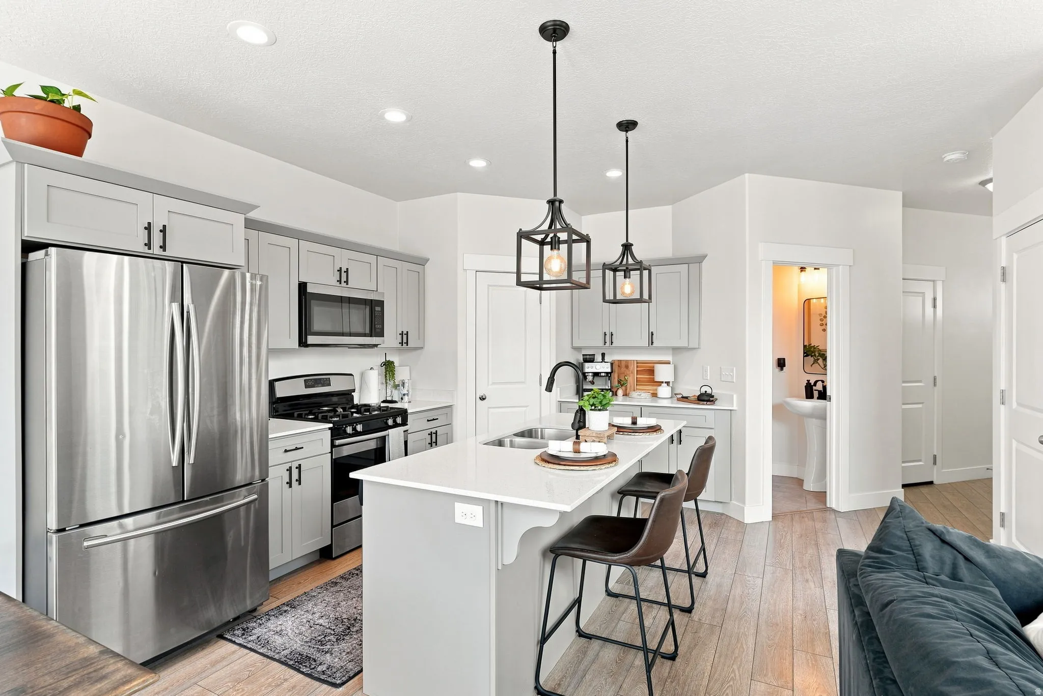 Modern kitchen featuring light gray cabinetry, stainless steel appliances, a center island with seating, and recessed and pendant lighting