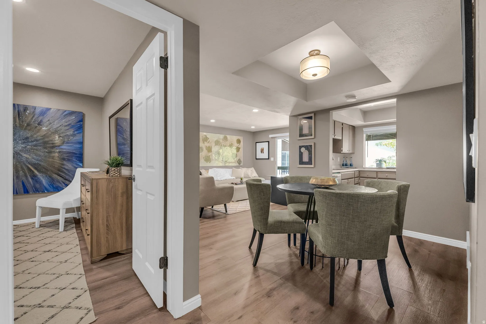 Recessed lighting, wood-finish flooring, tray ceiling with a semi-flush mount fixture, and a kitchen pass-through