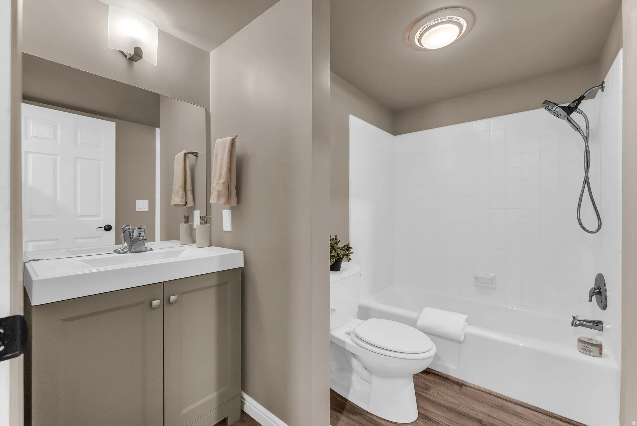 Wood-finish flooring, white bathtub with shower head, vanity with integrated sink, and wall-mounted mirror