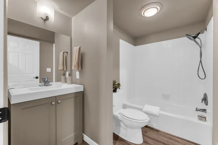 Wood-finish flooring, white bathtub with shower head, vanity with integrated sink, and wall-mounted mirror