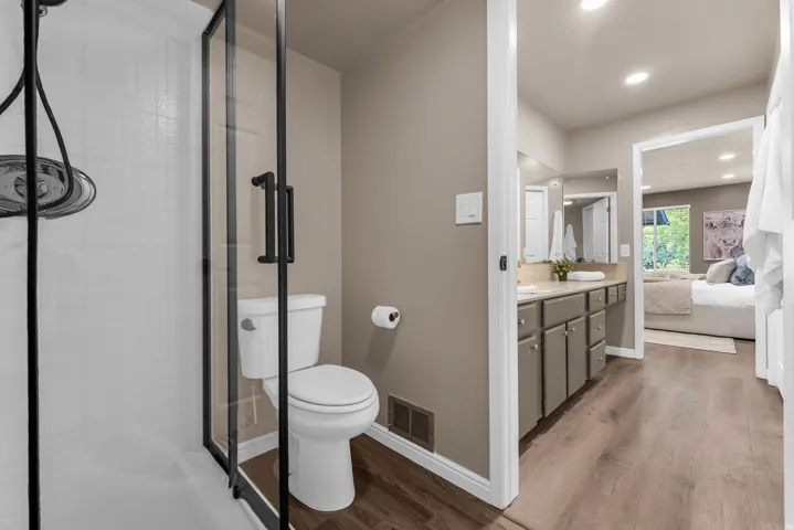 Glass-enclosed shower with a matte black frame, white tiled shower surround, dual vanity with undermount sinks, and wood-finish flooring