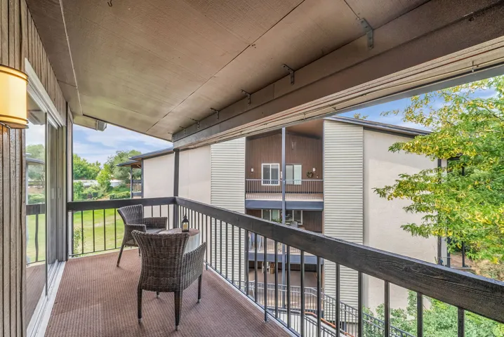 Private balcony featuring a textured floor covering, a metal railing, and an exterior wall light fixture