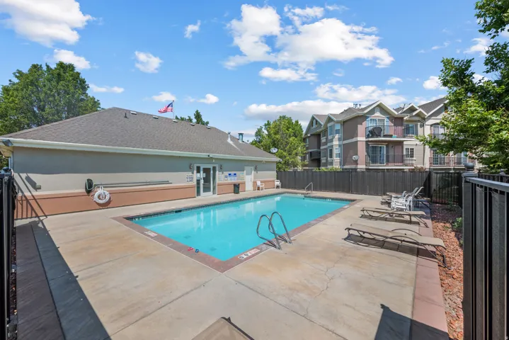Outdoor swimming pool with concrete decking, surrounded by a black metal fence