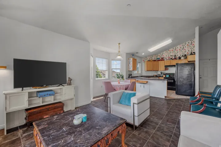 Open-concept living space with dark tile flooring, a kitchen featuring wood cabinetry, and a dining area with natural light from a window