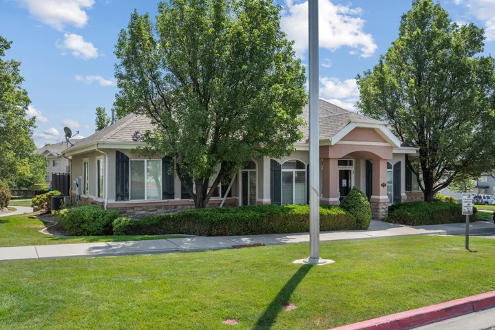 Stucco exterior with stone accent, arched entry, mature landscaping, and an asphalt shingle roof