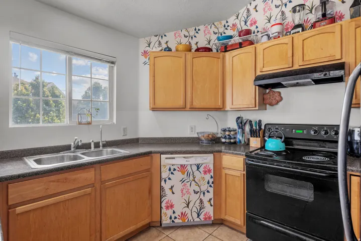Natural light kitchen featuring wood cabinetry, a dual basin stainless steel sink, black electric range, and dark countertops