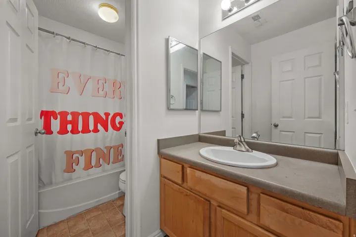 Bathroom featuring an integrated vanity sink with a two-door wood-finish cabinet, a built-in mirror, and a bathtub with a shower