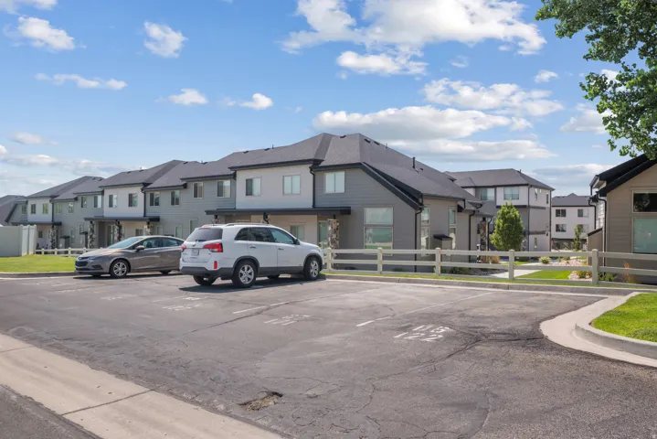 Modern multi-level townhomes featuring grey siding and dark roofs, complemented by a neatly maintained green lawn and a light-colored fence