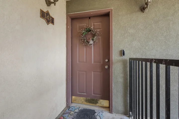 Entry door with a brass kick plate, textured stucco exterior, and a contemporary video doorbell