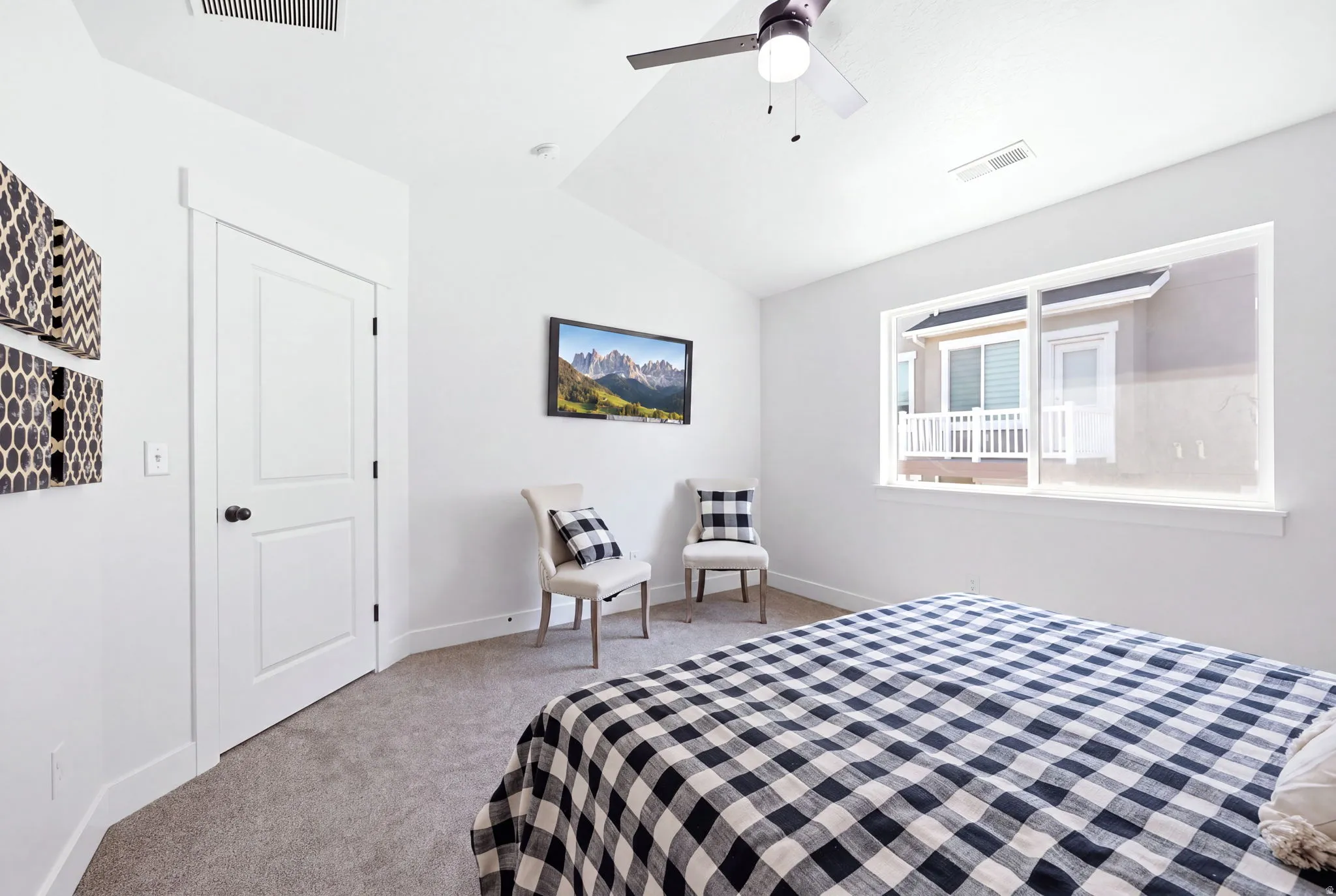 Spacious interior featuring a large window, vaulted ceiling, ceiling fan, white paneled door, and neutral-toned carpeting