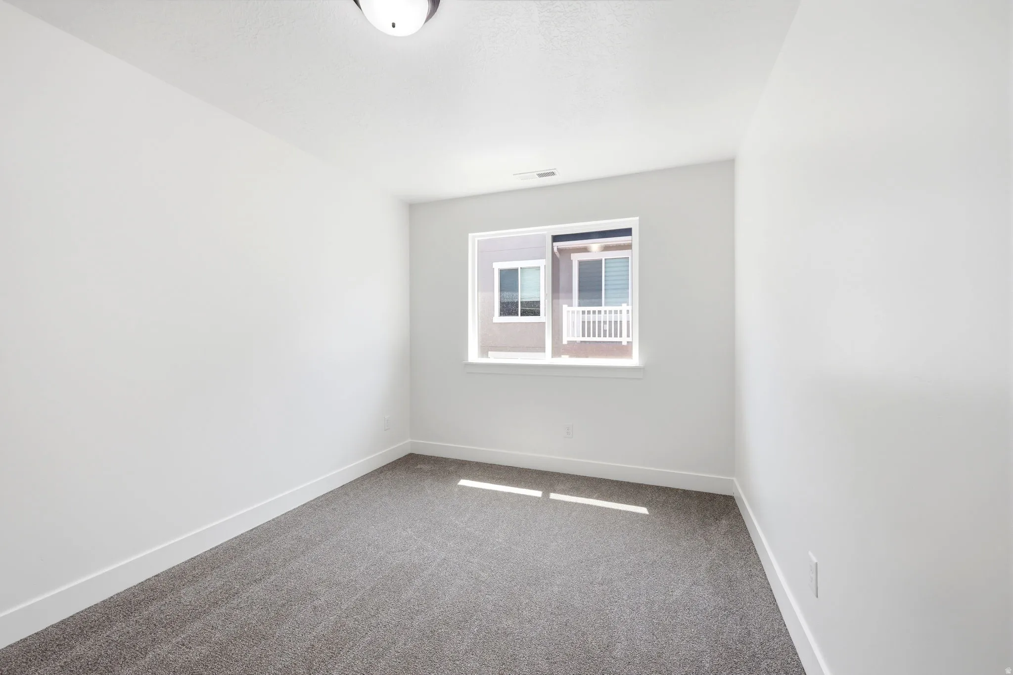 Bright room featuring a window with white trim, gray carpet flooring, white walls, and white baseboards
