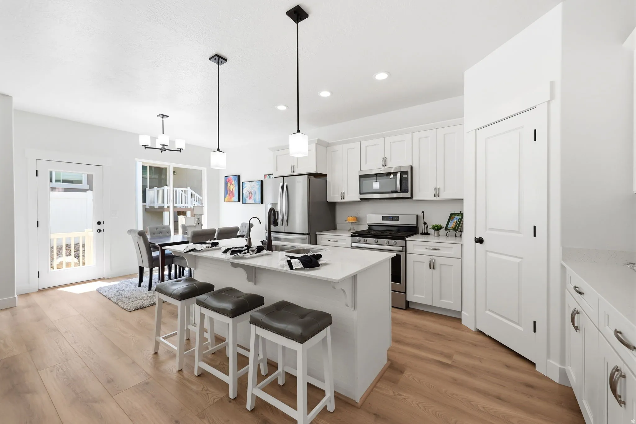 Open-concept kitchen and dining area featuring a large white kitchen island with waterfall countertop, seating for three, and pendant lighting overhead