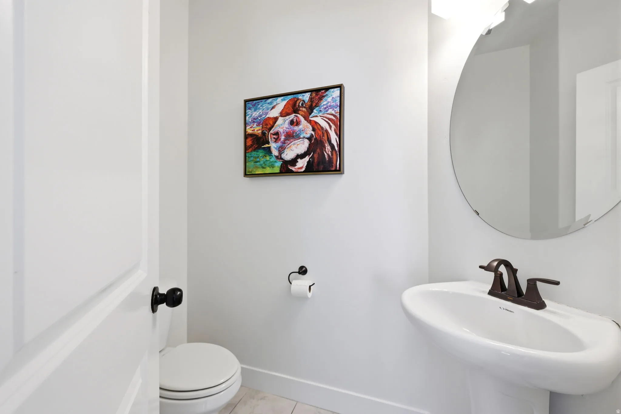 Pedestal sink with a bronze-finish faucet, accompanied by a round wall-mounted mirror