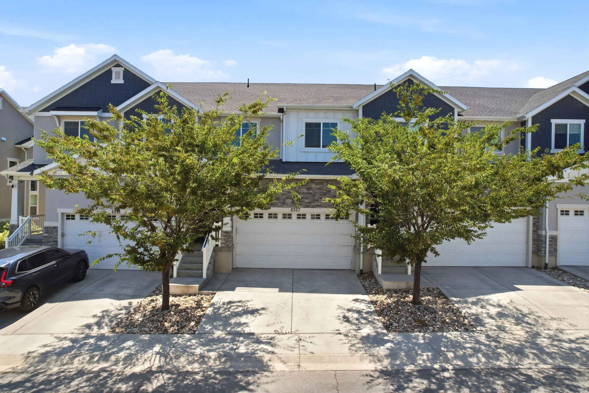 Townhome exterior featuring a combination of light-toned stucco and dark blue siding, stone veneer accents, and a two-car garage