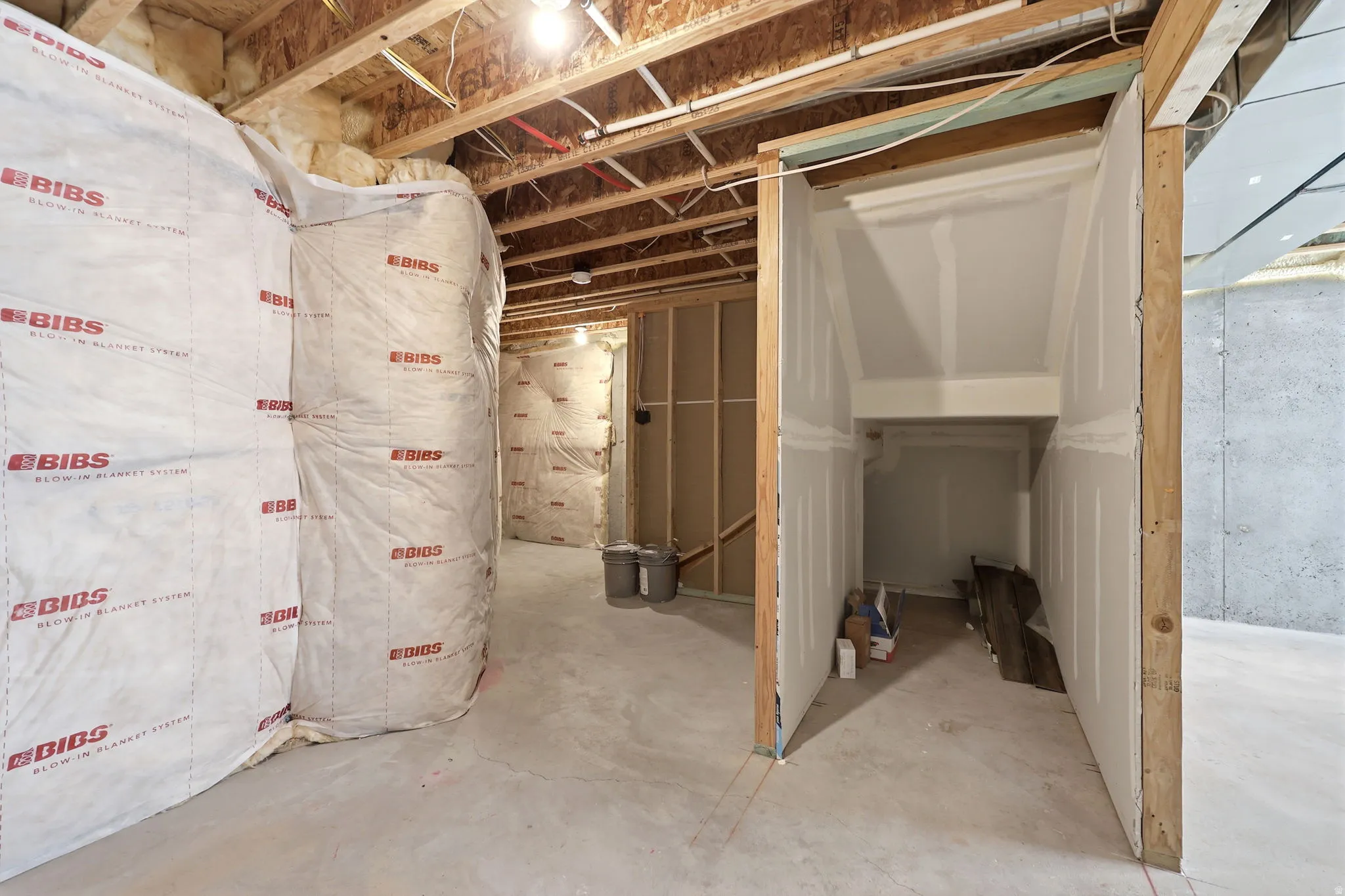 Unfinished basement space featuring visible insulation, exposed ceiling joists, concrete flooring, and framed walls