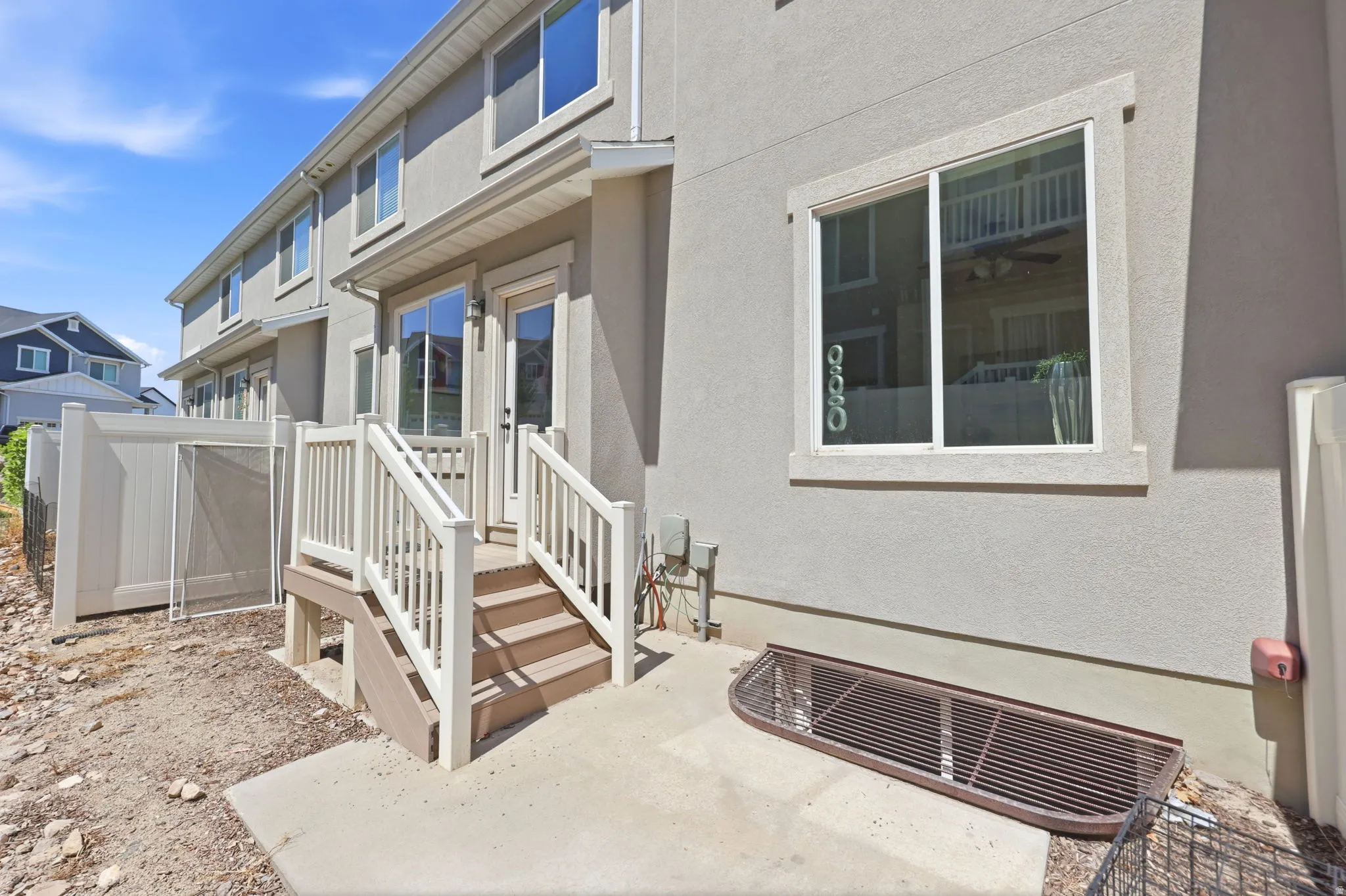 Rear exterior featuring a concrete patio, white vinyl fencing, and a deck with stairs providing access to the interior