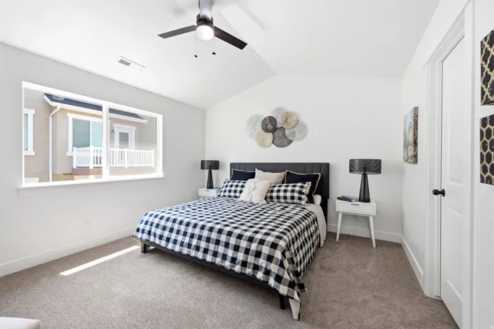Carpeted bedroom featuring a vaulted ceiling and a ceiling fan with integrated lighting